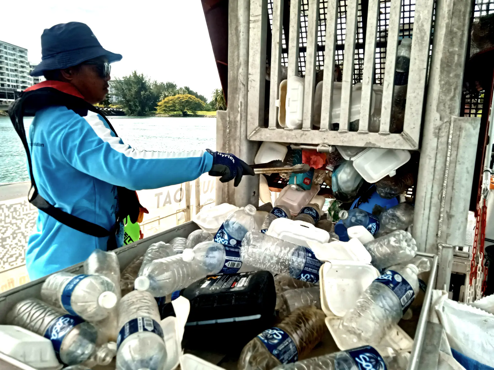 Person collecting plastic bottles from water on a boat